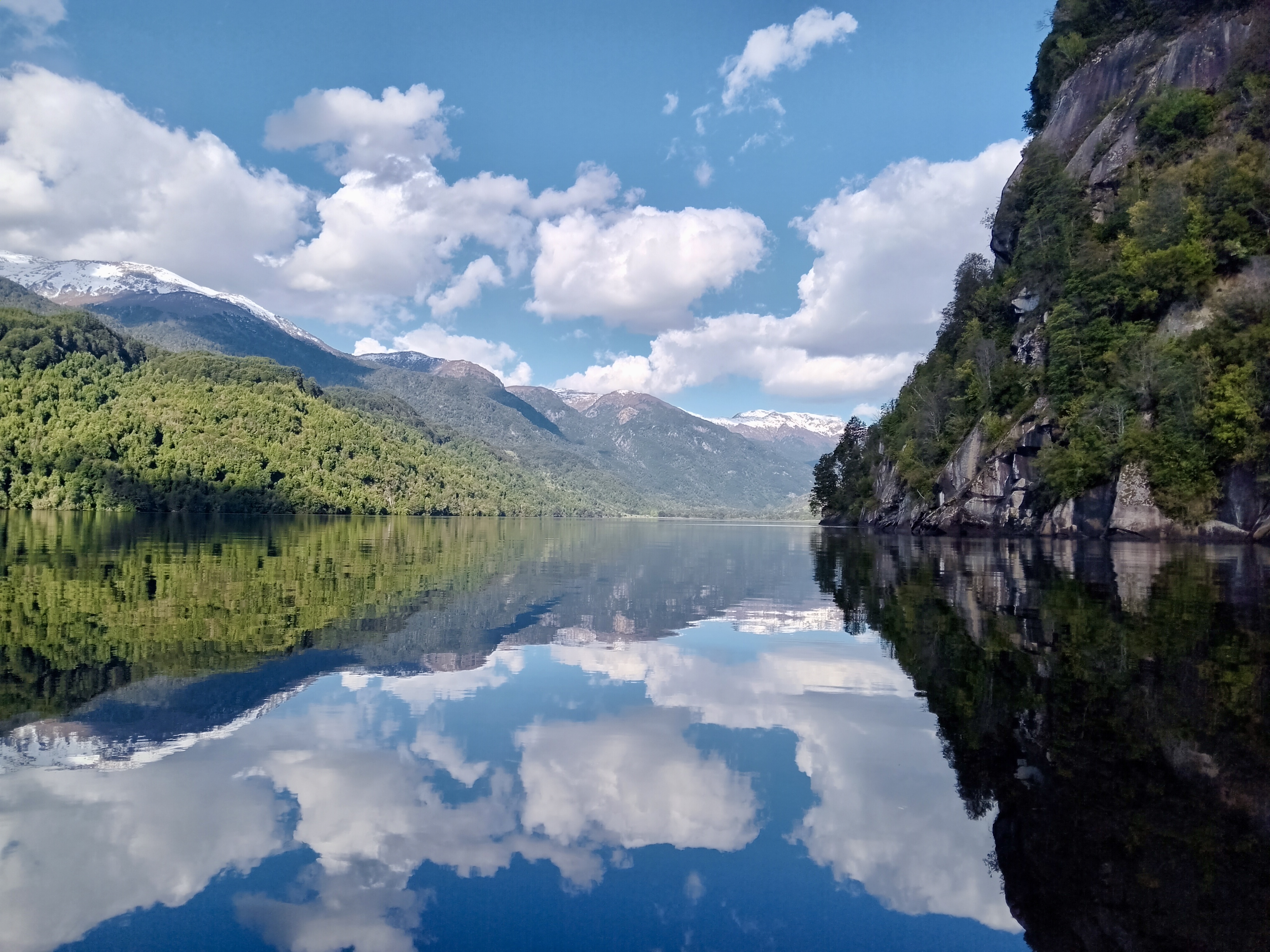 Acantilado y cordillera nevada reflejada en el lago